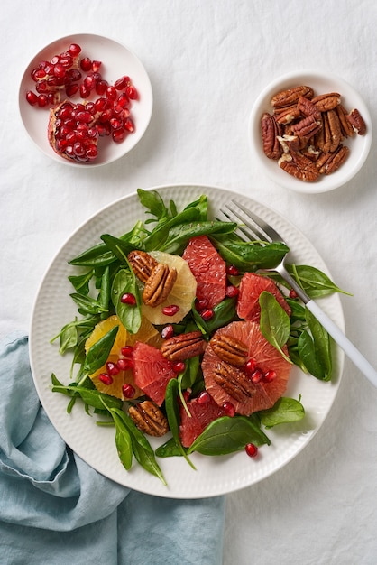 Vista superior da salada de frutas cítricas com nozes, folhas verdes de alface. Alimentação equilibrada. Espinafre com sementes de laranja, toranja, nozes e romã em uma tigela na mesa com uma toalha de mesa branca.