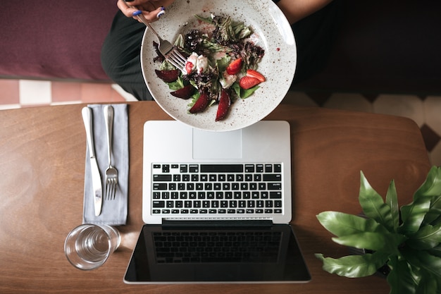 Vista superior da salada nas mãos e copo com faca e garfo na mesa do restaurante