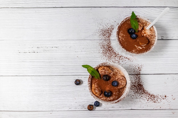 Vista superior da sobremesa clássica de tiramisu com biscoitos de cacau e savoyardi em potes de cerâmica brancos em cinza