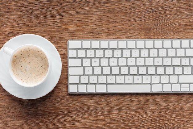 Vista superior da xícara de café e teclado portátil em fundo de madeira