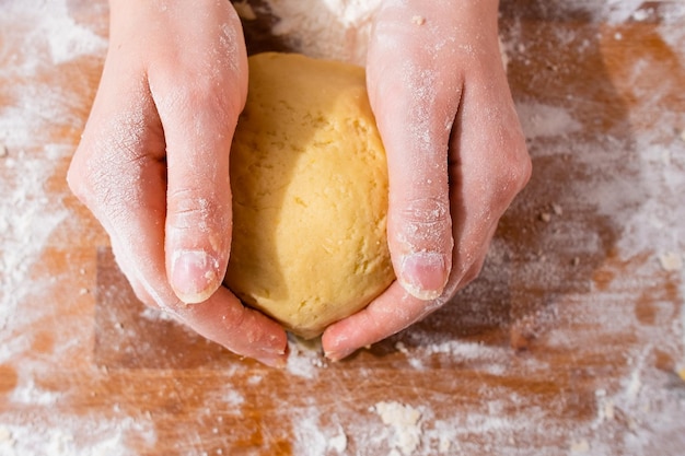 Vista superior das mãos da mulher amassando a massa para biscoitos de torta de pães ou pastelaria no processo de mesa de madeira