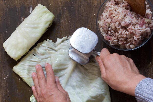 Vista superior das mãos da mulher batendo folha de repolho com amaciante de carne antes de encher no fundo marrom