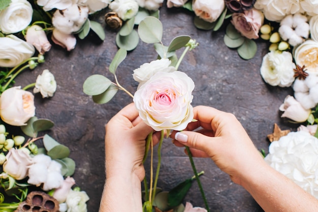 Vista superior das mãos da mulher com flores. A florista está fazendo uma composição de casamento elegante, design florístico