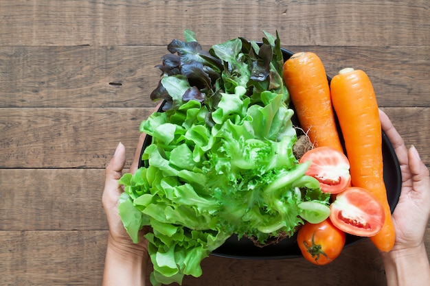 Foto vista superior das mãos da mulher segurando um prato de legumes frescos