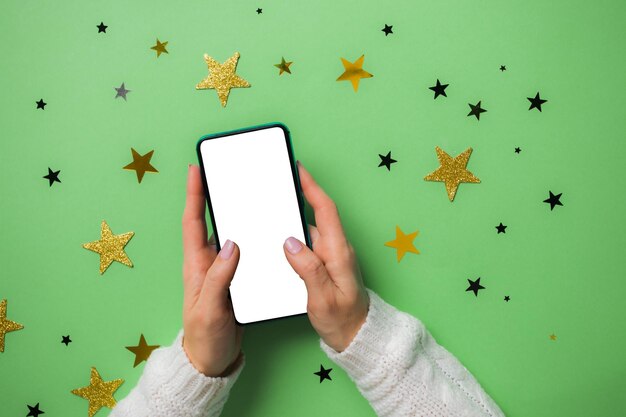 Vista superior das mãos da mulher sobre fundo verde com muitas estrelas douradas smartphone simulado nas mãos