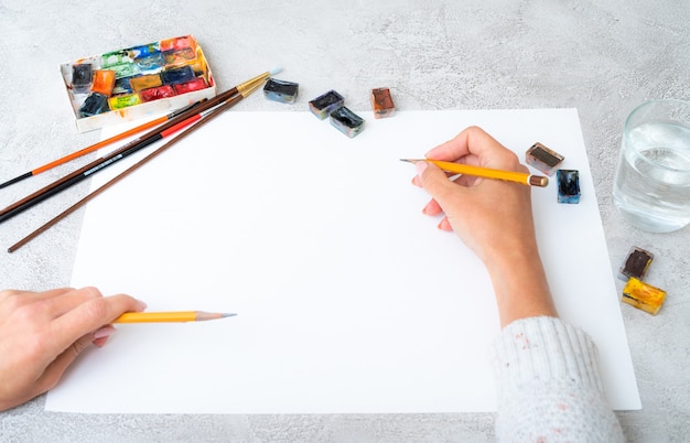 Vista superior das mãos de uma garota desenhando com lápis e tintas