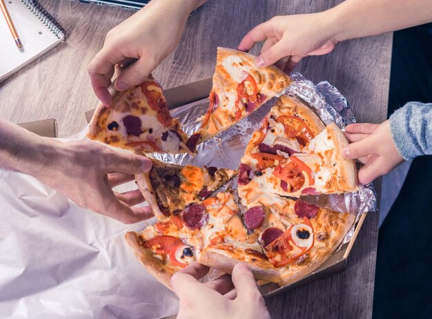 Vista superior das mãos pegando pizza. conceito de amizade no trabalho, união, trabalho em equipe, parceria.