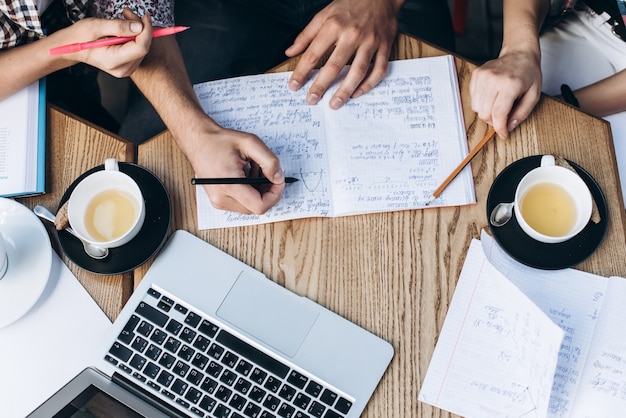 Vista superior das pessoas que estudam com caderno, livro e laptop. copos de café na mesa