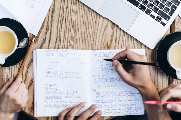 Vista superior das pessoas que estudam com caderno, livro e laptop. Copos de café na mesa