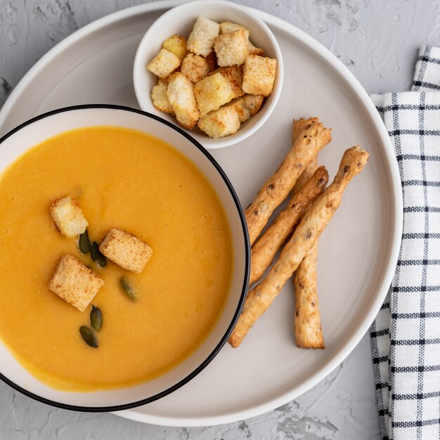 Vista superior de abóbora, sopa de creme de cenoura em uma tigela. com croutons, sementes de abóbora e palitos de pão.