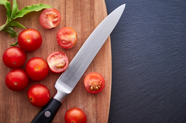 Vista superior de alguns tomates cereja com uma faca e uma mesa de madeira