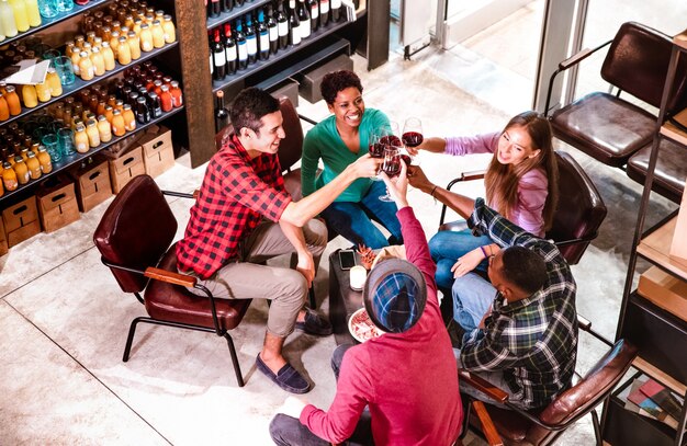 Vista superior de amigos ricos degustando vinho tinto e se divertindo na vinícola de um bar da moda