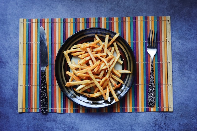 Vista superior de batatas fritas em um prato com talheres na mesa