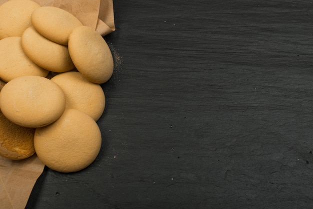 Vista superior de biscoitos caseiros redondos em fundo escuro. Cookies derramados com papel de embrulho