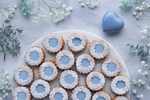 Vista superior de biscoitos Linzer de flores com vidros azuis em azul claro decorado com flores brancas e coração de cerâmica