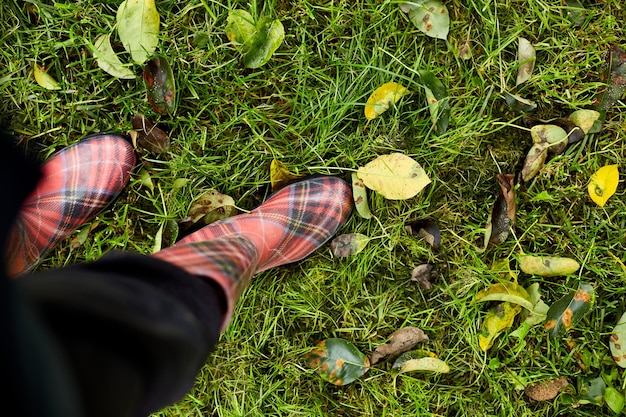 Vista superior de botas de borracha vermelhas brilhantes na grama com folhas de outono