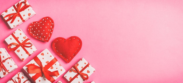 Vista superior de caixas de presente e corações têxteis vermelhos no conceito de dia de São Valentim de fundo colorido com espaço de cópia