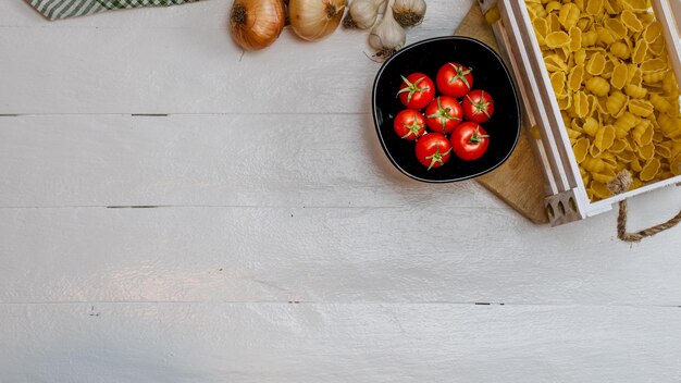 Foto vista superior de cebolas, massa de alho em uma caixa de madeira e tomates de cereja frescos maduros em uma mesa de madeira branca rústica ingredientes e conceito de comida