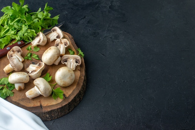 Vista superior de cogumelos crus e faca de verduras na placa de madeira, toalha branca no lado direito sobre fundo preto com espaço livre