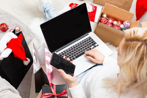 Vista superior de compras online de Natal. Compradora com laptop, copie o espaço na tela. Mulher toma café, compra presentes, prepara-se para a véspera de natal, sentada entre caixas e pacotes de presentes. Promoções de férias de inverno