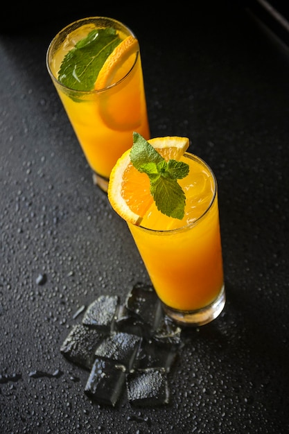 Vista superior de copos de suco de laranja com gelo derretendo em superfície preta