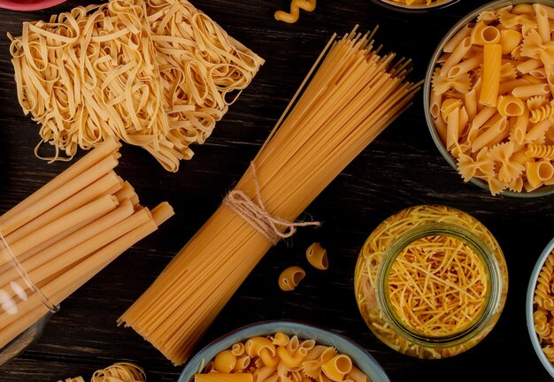 Foto vista superior de diferentes tipos de macarrão como bucatini, espaguete, vermicelli, tagliatelle e outros em fundo de madeira