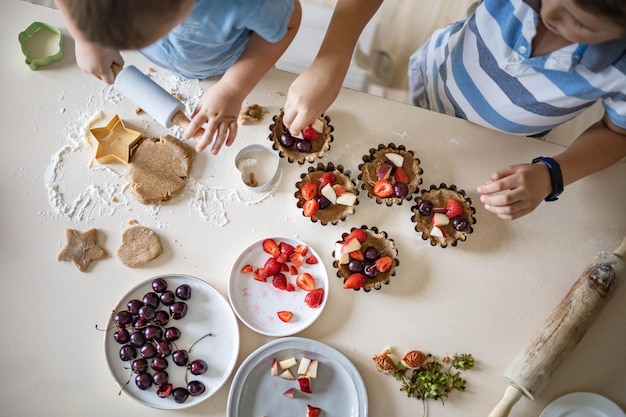 Vista superior de dois filhos do sexo masculino cozinhando sobremesa fresca de verão com massa e frutas maduras