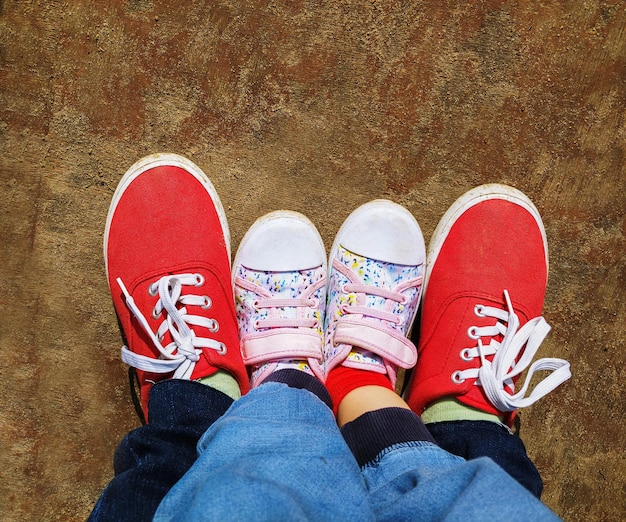 Vista superior de dois pares de pés em sapatos adultos e crianças em tênis vermelho e colorido na superfície de madeira