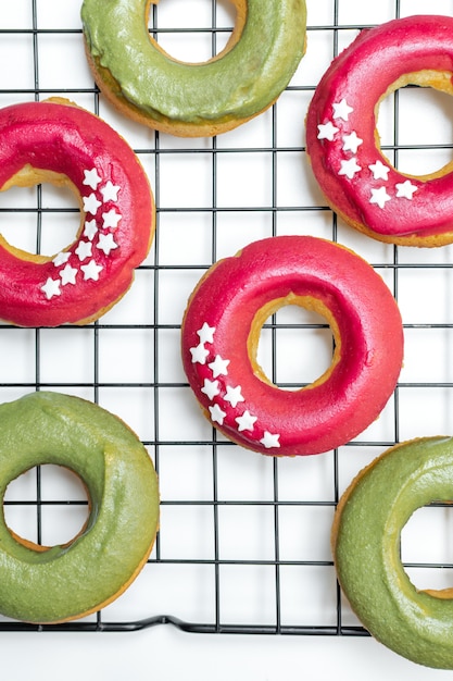 Vista superior de donuts cozidos frescos com glacê rosa e verde brilhante, star granulado na cremalheira de arrefecimento