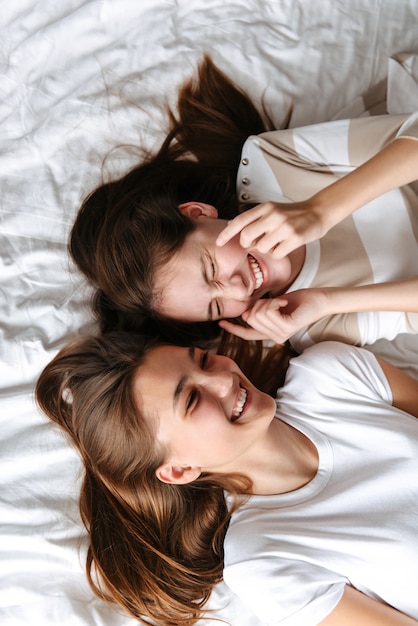 Vista superior de duas jovens adolescentes alegres, deitadas na cama, rindo