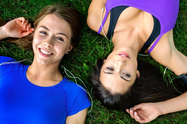 Vista superior de duas meninas bonitas e jovens descansando na grama após treino ao ar livre em um dia ensolarado