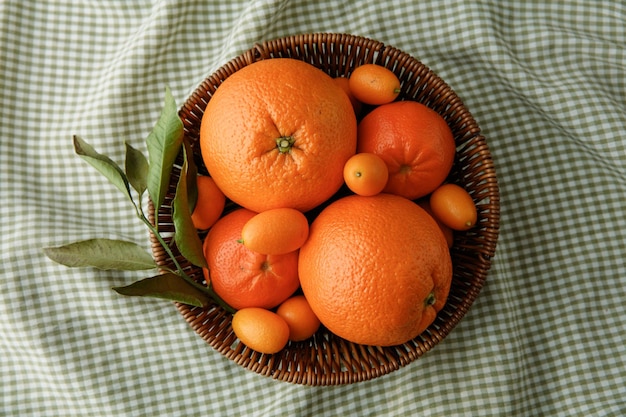 Vista superior de frutas cítricas como tangerina laranja e kumquat na cesta em fundo de pano xadrez