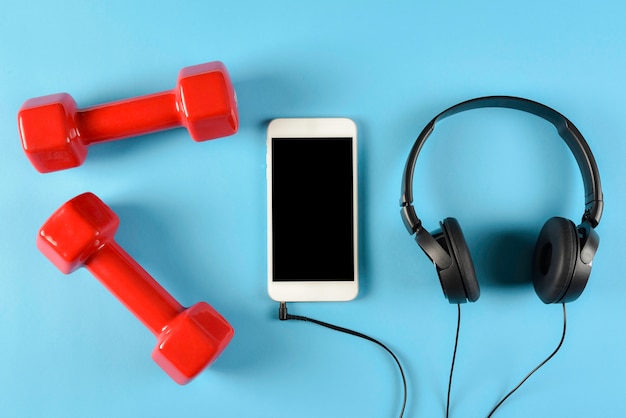 Vista superior de halteres vermelhos, fones de ouvido pretos e telefone inteligente. Conceito de música, esporte e fitness.