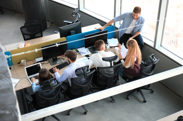 Vista superior de jovens colegas modernos em roupas casuais inteligentes, trabalhando juntos enquanto passam o tempo no escritório.