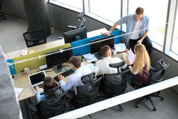 Vista superior de jovens colegas modernos em roupas casuais inteligentes, trabalhando juntos enquanto passam o tempo no escritório.