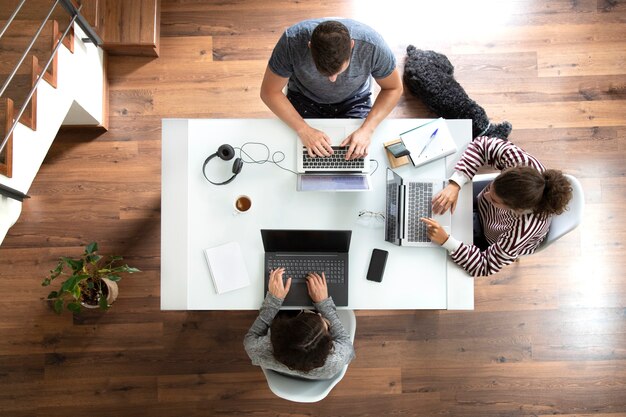 Vista superior de jovens trabalhando em casa usando laptops em uma mesa branca com um cachorro dormindo