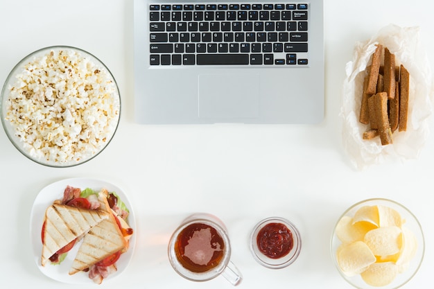 Vista superior de lanches e alimentos pouco saudáveis com o laptop na mesa branca, conceito de jogador