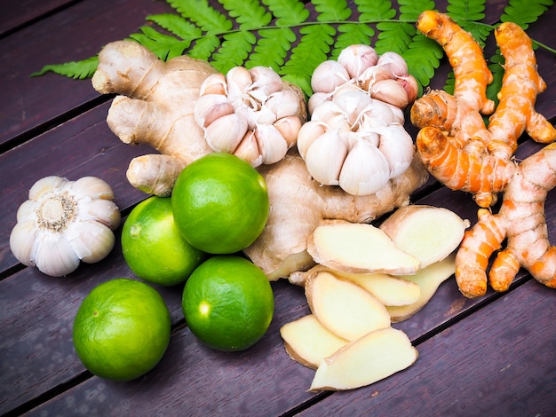 Vista superior de legumes e ervas para cozinhar com raiz de açafrão, gengibre, alho e limão frutas em folhas de samambaia na mesa de madeira na cozinha.