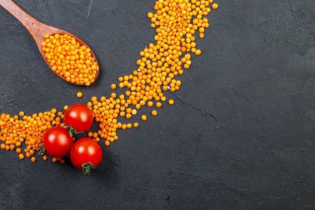 Vista superior de lentilhas vermelhas alinhadas em um círculo e tomates em fundo preto com espaço livre