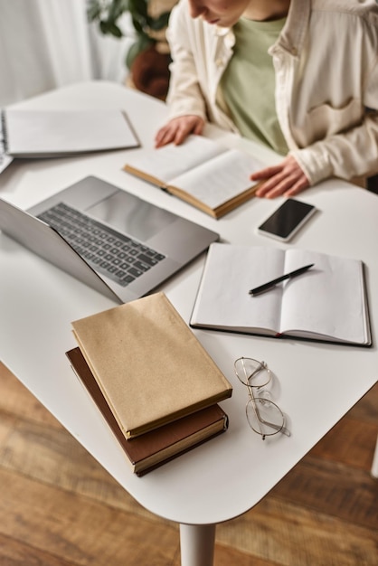 vista superior de livros e artigos de escritório em uma mesa de trabalho perto de uma adolescente concentrada fazendo a lição de casa