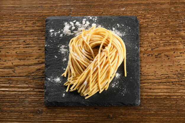 Vista superior de macarrão com ovo de alla chitarra italiano cru feito à mão espaguete feito à mão em uma lousa polvilhada com farinha colocada na mesa de madeira