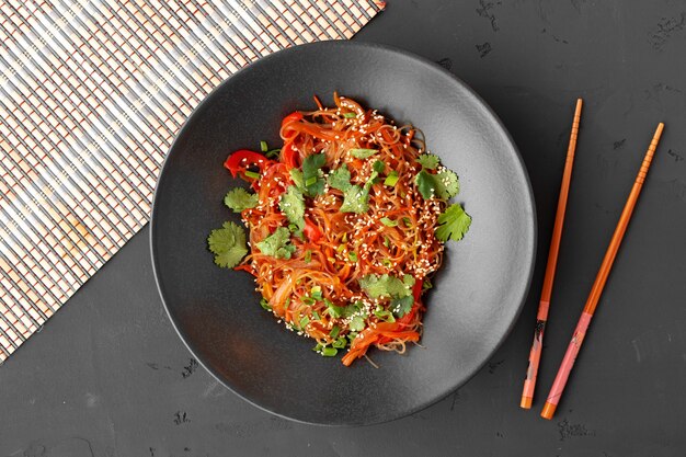 Vista superior de macarrão wok com legumes e carne em uma tigela sobre fundo cinza