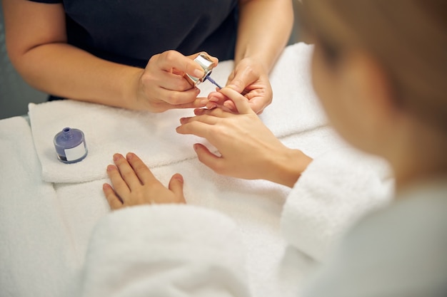 Vista superior de mãos femininas enquanto a artista faz as unhas coloridas com esmalte de gel