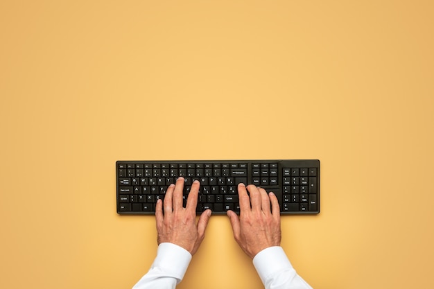 Vista superior de mãos masculinas digitando no teclado preto do computador sobre o amarelo