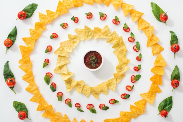 Foto vista superior de molho de pimentas picadas e nachos saborosos com folhas de manjericão e tomates cereja