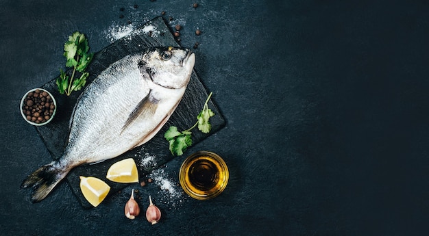 Vista superior de peixe dourado cru com azeite de oliva de especiarias verdes em uma tigela com limão cortado em um fundo de concreto preto com espaço livre para a massa