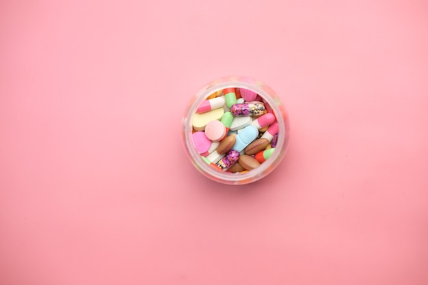vista superior de pílulas coloridas em um recipiente em fundo rosa