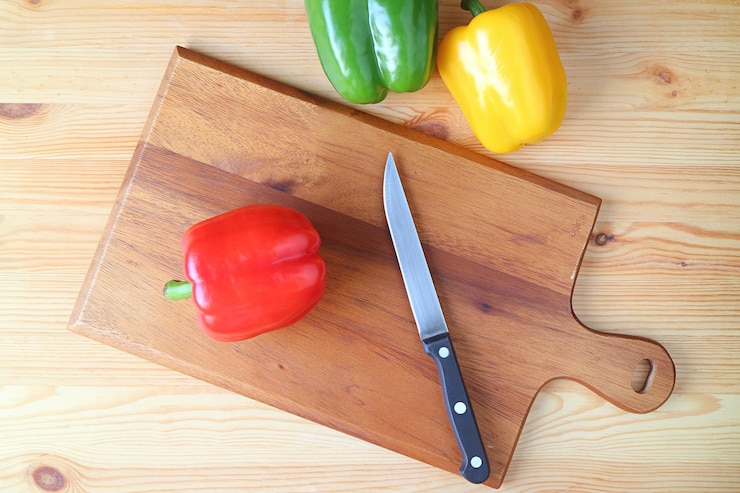 Foto vista superior de pimenta vermelha em uma tábua de corte com uma faca e duas pimentas em uma mesa de madeira