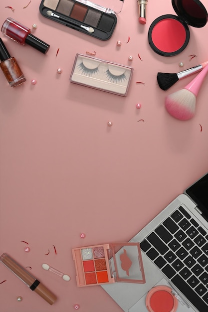 Vista superior de pincéis de maquiagem para laptop e cosméticos em fundo rosa Espaço de trabalho feminino