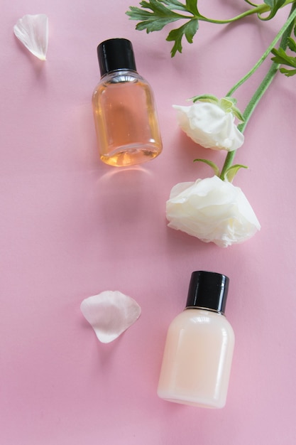 Vista superior de produtos cosméticos e flores delicadas em fundo rosa. Tratamento de beleza de bem-estar. Produtos orgânicos para o cuidado da pele